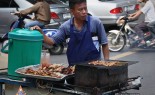 在一个繁忙的十字路口，泰国街头小贩在木炭烧烤车上卖各种串和糯米饭。