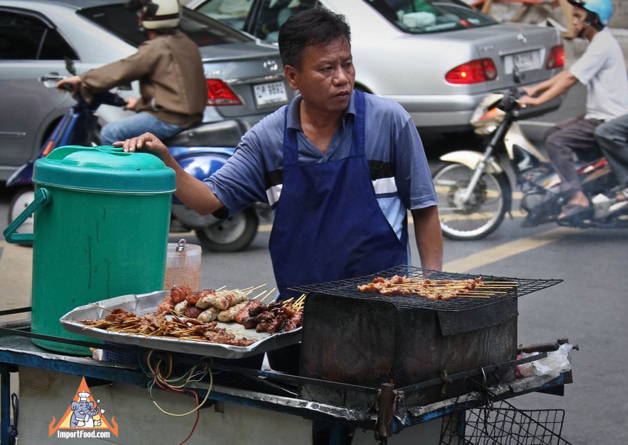 泰国街的供应商在繁忙的十字路口的木炭烧烤推车上搭配各种串烤米饭和粘性米饭。